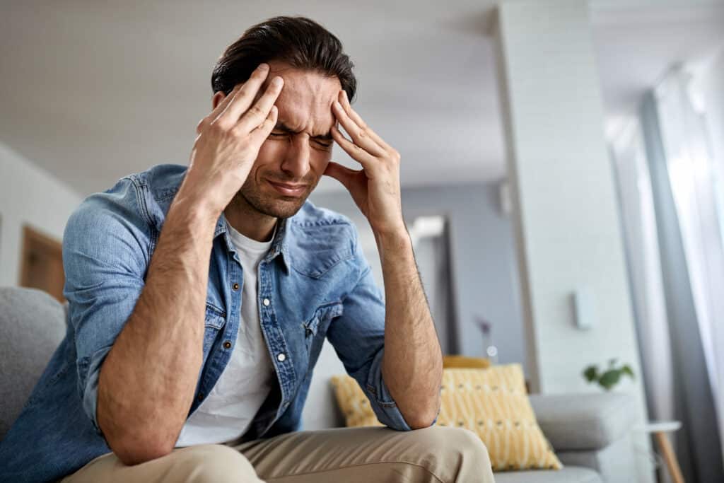 low angle view distraught man holding his head pain while sitting living room Four signs a first responder may be suffering from post traumatic stress