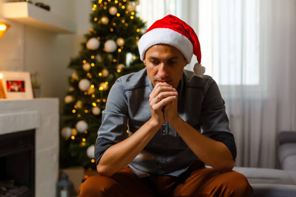 christmas time lonely man praying xmas wall with lights hung christmas tree festive mood home winter First Responder Grief During the Holidays